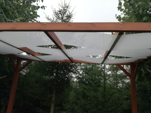 Bande d'ombrage de pavillon blanche entrelacée à travers la structure en bois d'une pergola de jardin