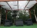 Witte schaduwdoek voor prieel gemonteerd op een houten pergola boven een tuinstel op het terras