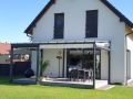 Rulou roman alb pentru terasă 2,5x4 m montat pe o pergolă grafit lângă o casă modernă cu grădină