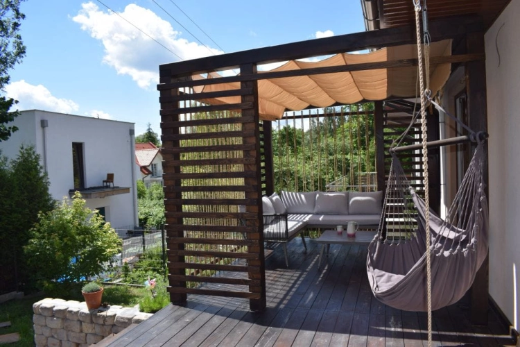 Store romain de terrasse beige 3x3 m monté sur une pergola en bois avec hamac et mobilier de jardin