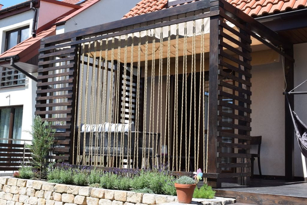 Waterdicht Premium vouwgordijn voor terras in beige gemonteerd op een houten pergola met decoratieve touwen