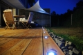 Vela de sombra triangular Premium impermeable instalada en una terraza con focos y muebles al anochecer