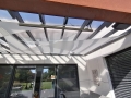 Toldo vela triangular Premium impermeable instalado bajo un techo de terraza acristalado.