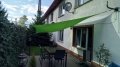 Toldo vela verde de 3x3 m instalado sobre una terraza con muebles de jardín junto a la casa
