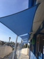 Toldo vela azul 4x4 solar e impermeable instalado sobre el pasillo junto al edificio