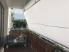 Vela ombreggiante Premium impermeabile montata su un balcone sopra un divano grigio, a protezione dal sole