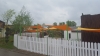 Vela de sombra triangular naranja Premium instalada sobre un parque infantil detrás de una valla blanca