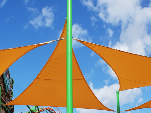 Toldo vela triangular naranja Premium montado en un poste verde alto junto a la piscina