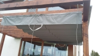 Store romain de terrasse gris 4x4 m monté sur câbles sous une pergola en bois, protection solaire premium