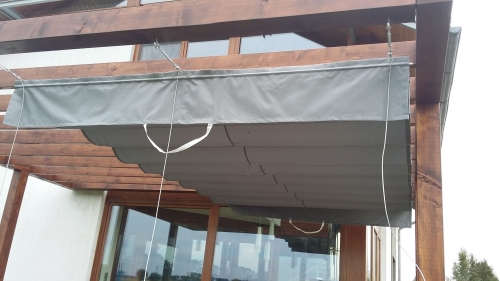 Store romain de terrasse gris 4x4 m monté sur câbles sous une pergola en bois, protection solaire premium