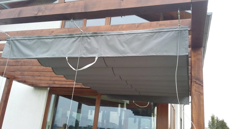 Store romain de terrasse gris 4x4 m monté sur câbles sous une pergola en bois, protection solaire premium