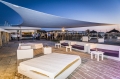 Voile d'ombrage triangulaire blanche au-dessus d'une terrasse avec mobilier de jardin au bord de la plage au crépuscule