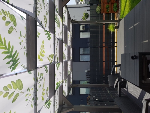 Bande de pavillon imperméable avec imprimé feuilles vertes installée comme pare-soleil sur la structure d'une tonnelle