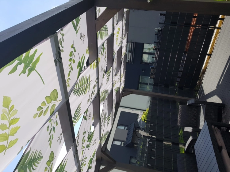 Voile d'ombrage imperméable pour tonnelle avec motif de feuilles vertes, monté sur une pergola en bois