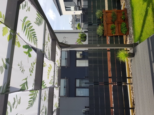 Bande de store imperméable avec imprimé feuilles de fougère, installée sur une pergola de terrasse.