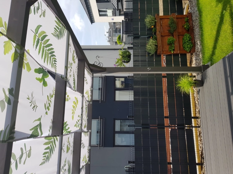 Bande de store imperméable avec imprimé feuilles de fougère, installée sur une pergola de terrasse.