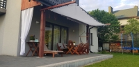 Biela výsuvná tieniaca plachta chrániaca záhradný nábytok na terase s drevenou konštrukciou