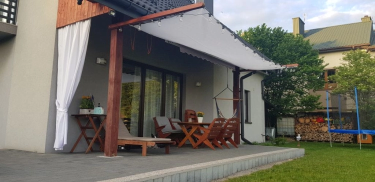 Biela výsuvná tieniaca plachta chrániaca záhradný nábytok na terase s drevenou konštrukciou