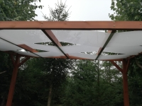 Wit zonnezeil gemonteerd op een houten pergola in een groene tuin