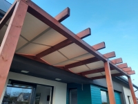 Bande romaine imperméable sur mesure montée sur une pergola de terrasse en bois protégeant du soleil