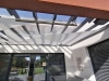 Toldo vela triangular blanco instalado bajo un techo de terraza acristalado como protección solar