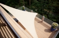Toldo vela triangular impermeable Premium en color beige instalado en una terraza con vistas al bosque