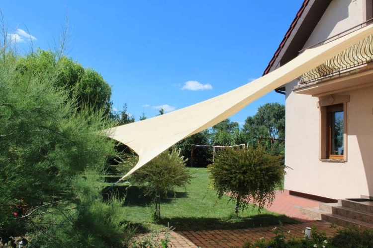 Beżowy kwadratowy żagiel przeciwsłoneczny 5x5 m HDPE zamontowany nad tarasem w ogrodzie przy domu jednorodzinnym