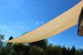 Beżowy żagiel przeciwsłoneczny 4x7 m z materiału HDPE zamontowany nad tarasem w słoneczny dzień