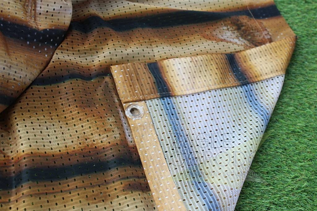 Gros plan sur un rideau de jardin imprimé, structure en maille du matériau et œillet de montage métallique visibles