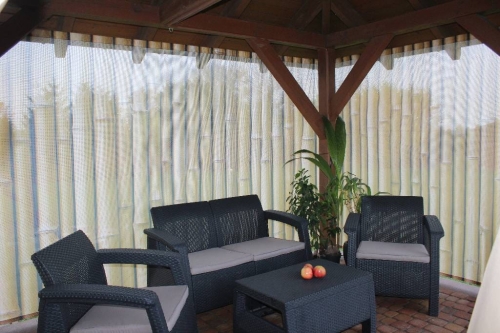 Rideau de jardin avec imprimé de pousses de bambou dans une tonnelle avec des meubles en rotin foncé et des plantes en pot