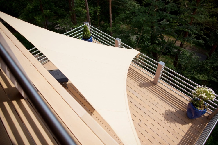 Toldo vela triangular beige instalado sobre una terraza de suelo compuesto con barandilla