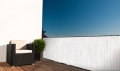 Protección de balcón blanca a medida con estampado de madera, montada en la barandilla de la terraza con mueble de jardín