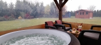 Przeźroczysta plandeka na wymiar osłaniająca taras z widokiem na ogród, przy którym stoi jacuzzi i meble ogrodowe