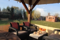 Przezroczysta plandeka na taras zamontowana na drewnianej altanie z widokiem na ogród i domek narzędziowy