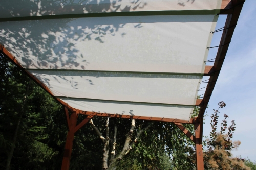 Maßgefertigtes weißes Sonnensegel an einer Holzpergola im Garten montiert.