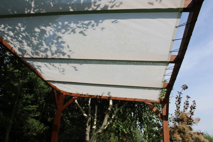 Maßgefertigtes weißes Sonnensegel an einer Holzpergola im Garten montiert.