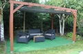 Toldo vela retráctil gris de HDPE bajo una pérgola de madera con muebles de jardín sobre suelo verde