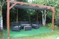 Graues ausziehbares HDPE-Sonnensegel unter einer Holzpergola mit Gartenmöbeln auf grünem Untergrund