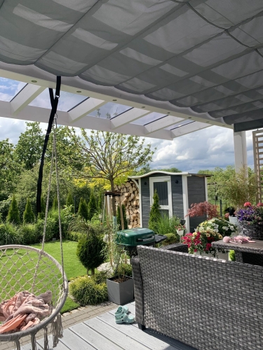 Store banne horizontal gris sur mesure installé sous le toit vitré d'une terrasse de jardin moderne