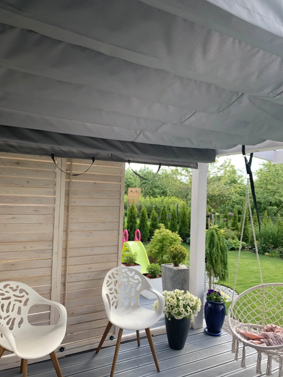 Store romain horizontal gris sur mesure installé sous le toit de la terrasse dans un jardin d'hiver