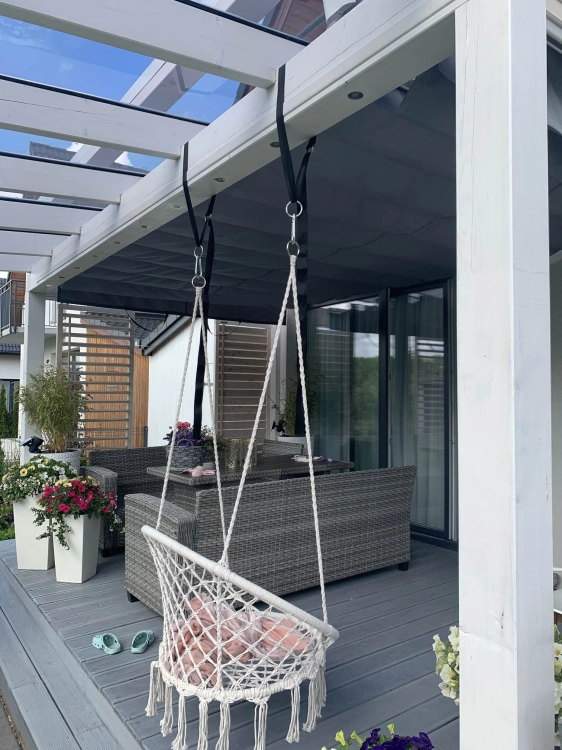 Store banne horizontal gris sous un toit de terrasse en poutres blanches avec fauteuil suspendu et mobilier de jardin
