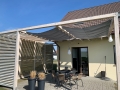 Vela ombreggiante grigia impermeabile estensibile montata su una pergola in legno sopra il terrazzo con mobili da giardino