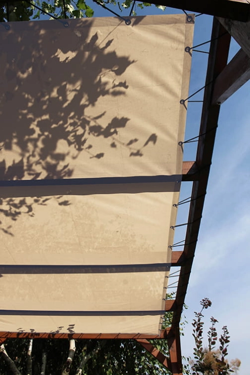 Voile d'ombrage beige HDPE sur mesure montée sur une pergola en bois avec des cordes élastiques