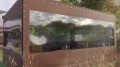 Lona marrón a medida con gran ventana transparente que protege la terraza de jardín contra la lluvia y el viento