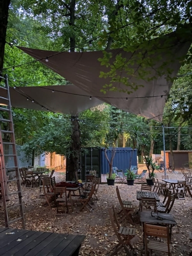 Voile d'ombrage triangulaire imperméable en PVC au-dessus de tables en bois dans un jardin de restaurant en automne