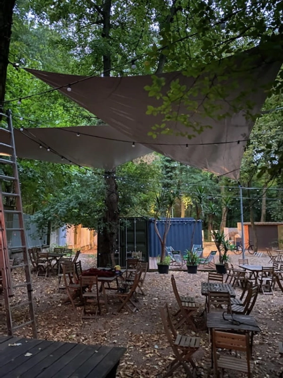 Voile d'ombrage triangulaire imperméable en PVC au-dessus de tables en bois dans un jardin de restaurant en automne
