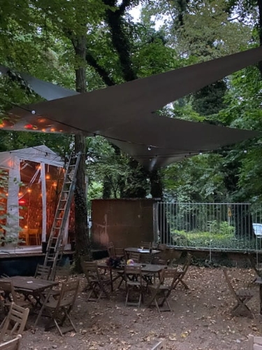 Voile d'ombrage triangulaire imperméable en PVC sur mesure installée au-dessus des tables d'un jardin de restaurant