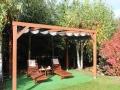 Graues wasserdichtes PVC-Faltrollo für die Terrasse, montiert an einer Holzpergola im Garten mit Liegestühlen