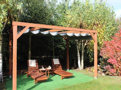 Store romain de terrasse gris en PVC imperméable monté sur une pergola en bois dans un jardin avec transats