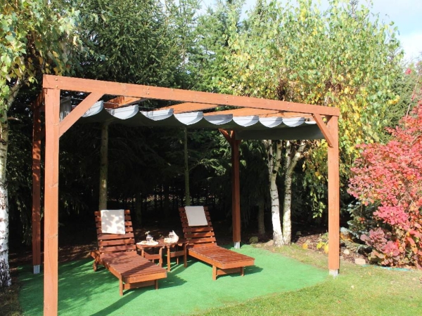 Grijs waterdicht PVC-vouw-terrasgordijn gemonteerd op een houten pergola in de tuin met ligstoelen